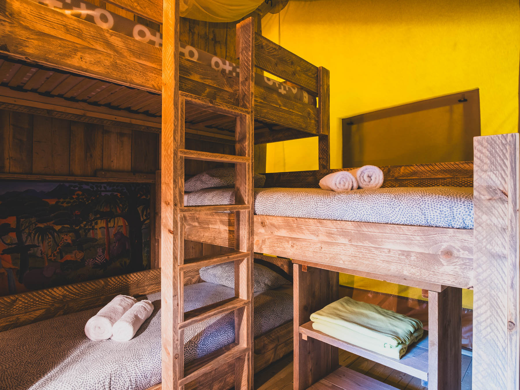 Wooden bunk beds with patterned bedding and rolled towels in a room with yellow walls.
