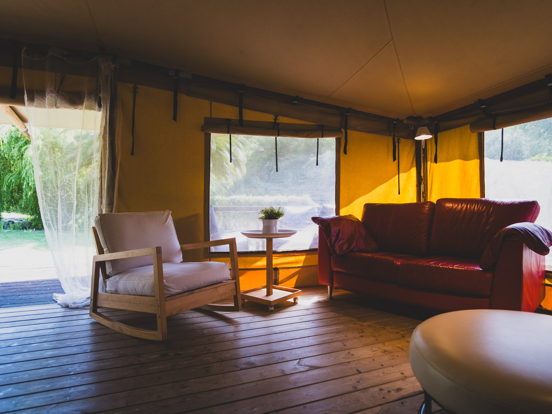 Interior of a tent with wooden flooring, red sofa, white cushioned chair, small table, and yellow walls.