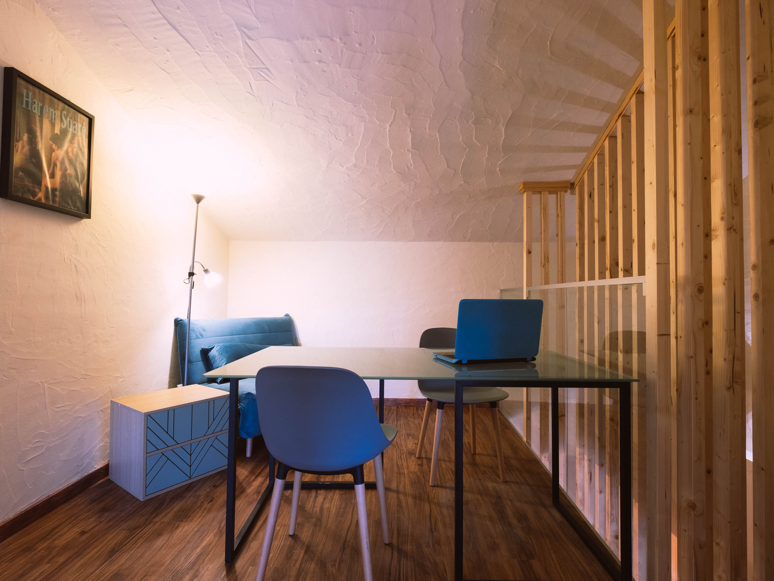 Room with a table, three chairs, a couch, a laptop, and a wall lamp under a curved ceiling.