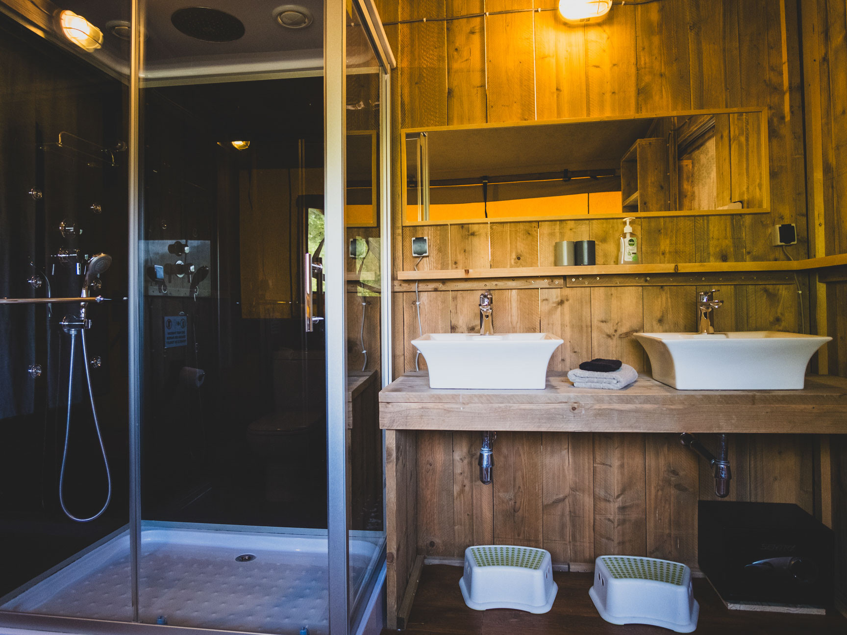 Bathroom with wooden paneling, two white sinks, a large mirror, and a glass-enclosed shower area.