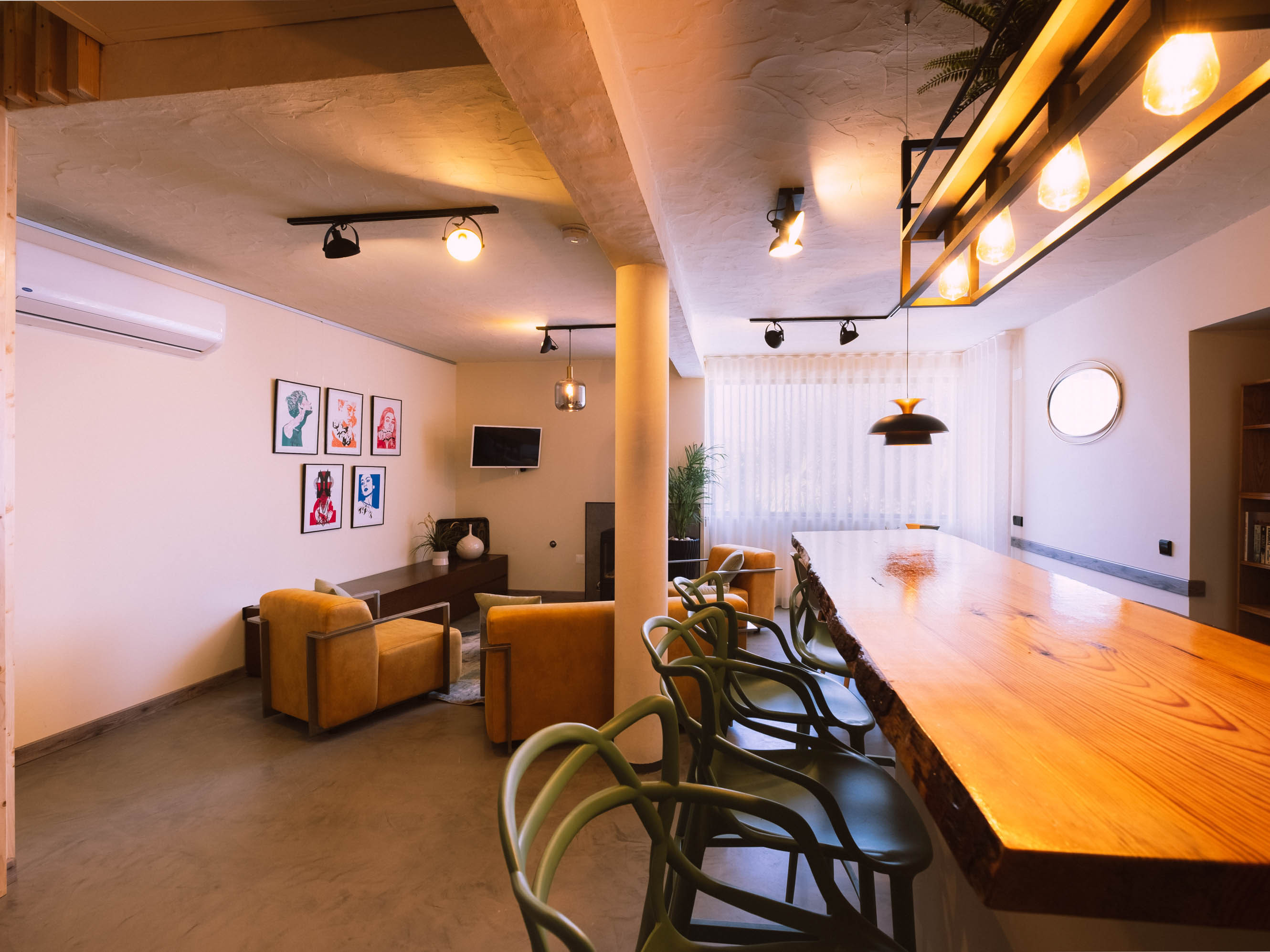 Living room with yellow armchairs, a wooden dining counter, black chairs, framed art, and overhead lights.