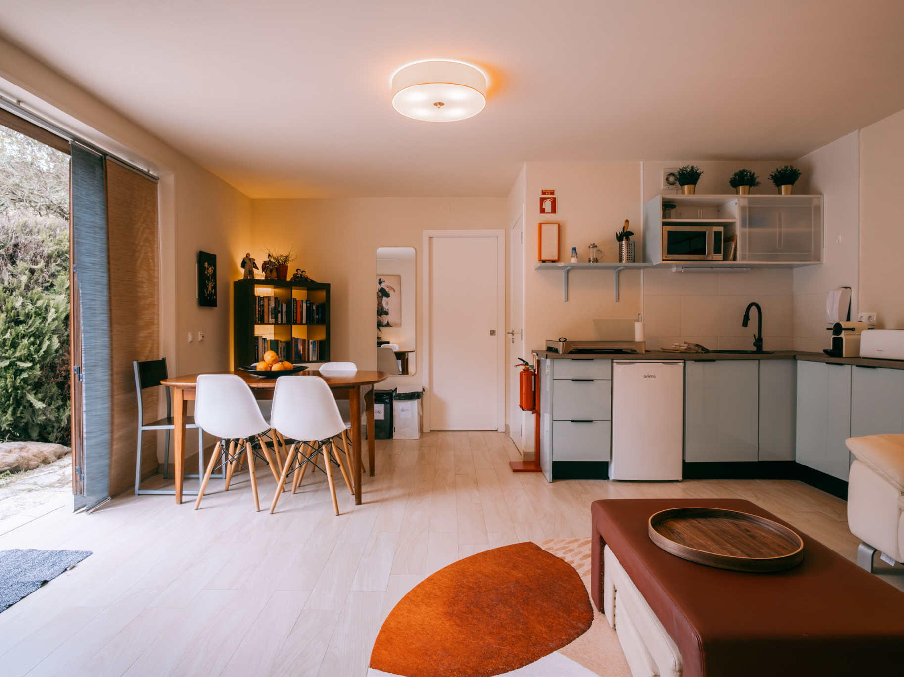 Open-plan living area with dining table, chairs, kitchenette, and sliding door to a garden.