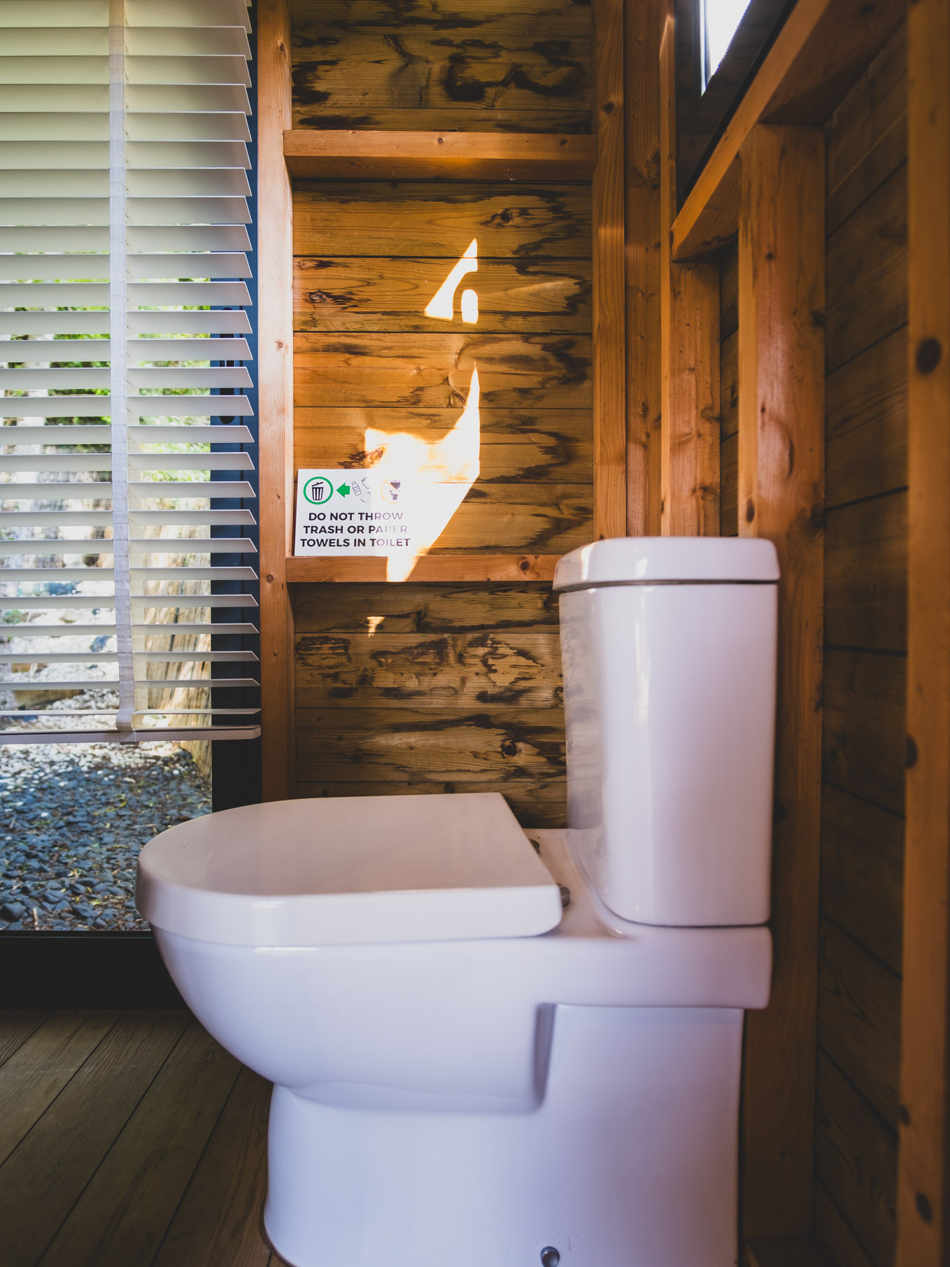White toilet in a wooden bathroom with a sign about proper waste disposal on the wall.