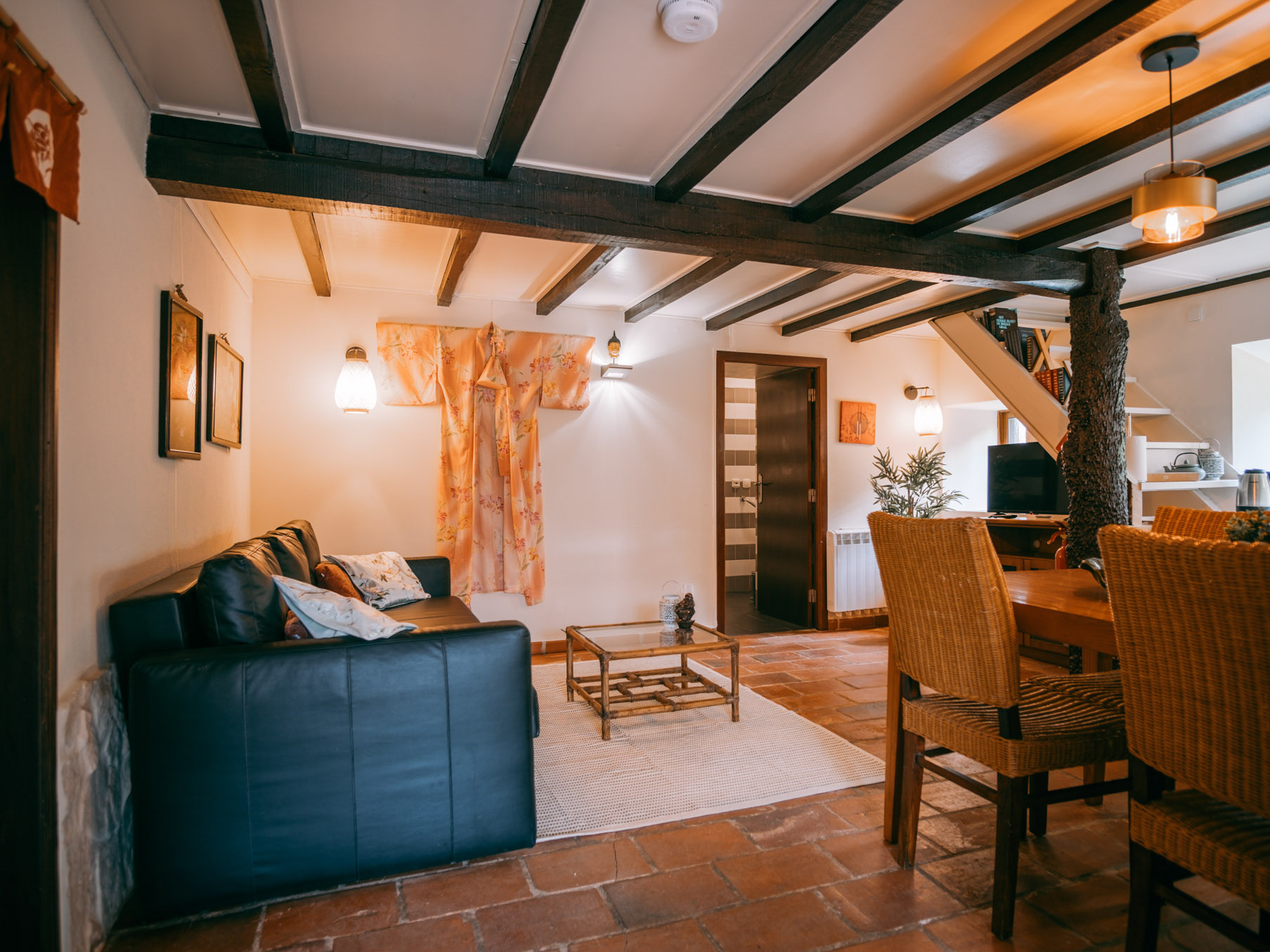 Living room with black sofa, a table on a light rug, woven chairs, wooden beams, and a decorated