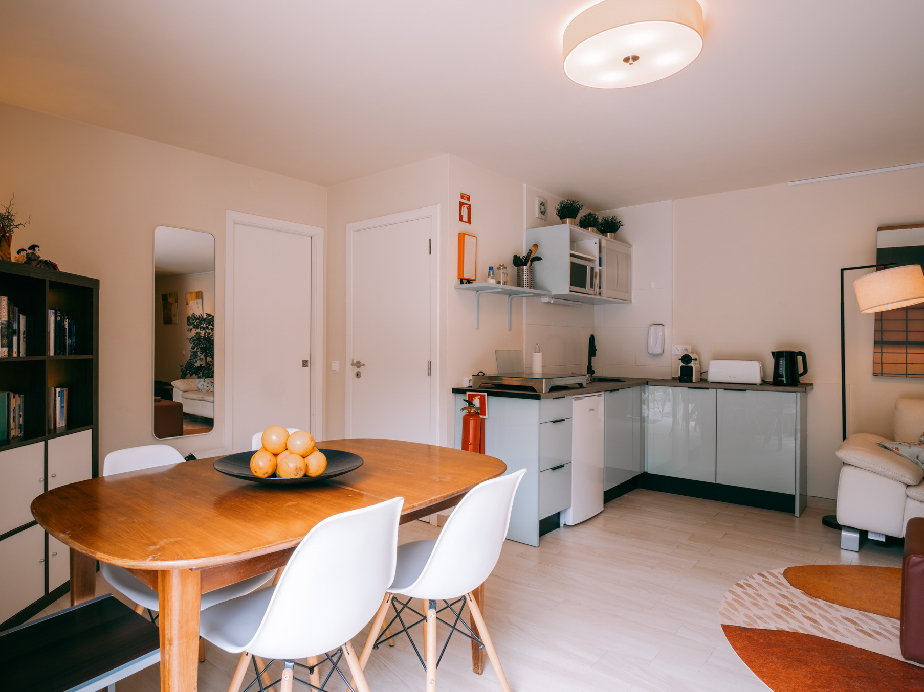 Dining table with white chairs and bowl of oranges in open-plan kitchen living area.
