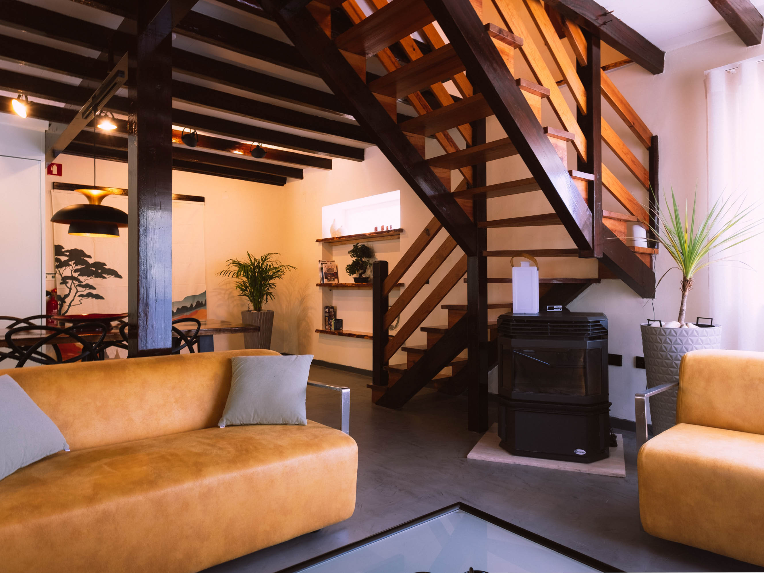 Living room with leather sofas, a glass coffee table, wooden stairs, and indoor plants near window.