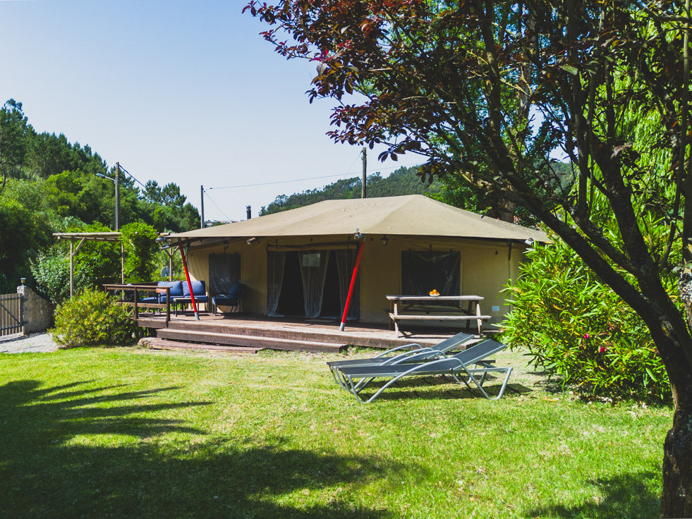 Tent structure with a covered porch, wooden deck, picnic table, and two lounge chairs on grassy lawn