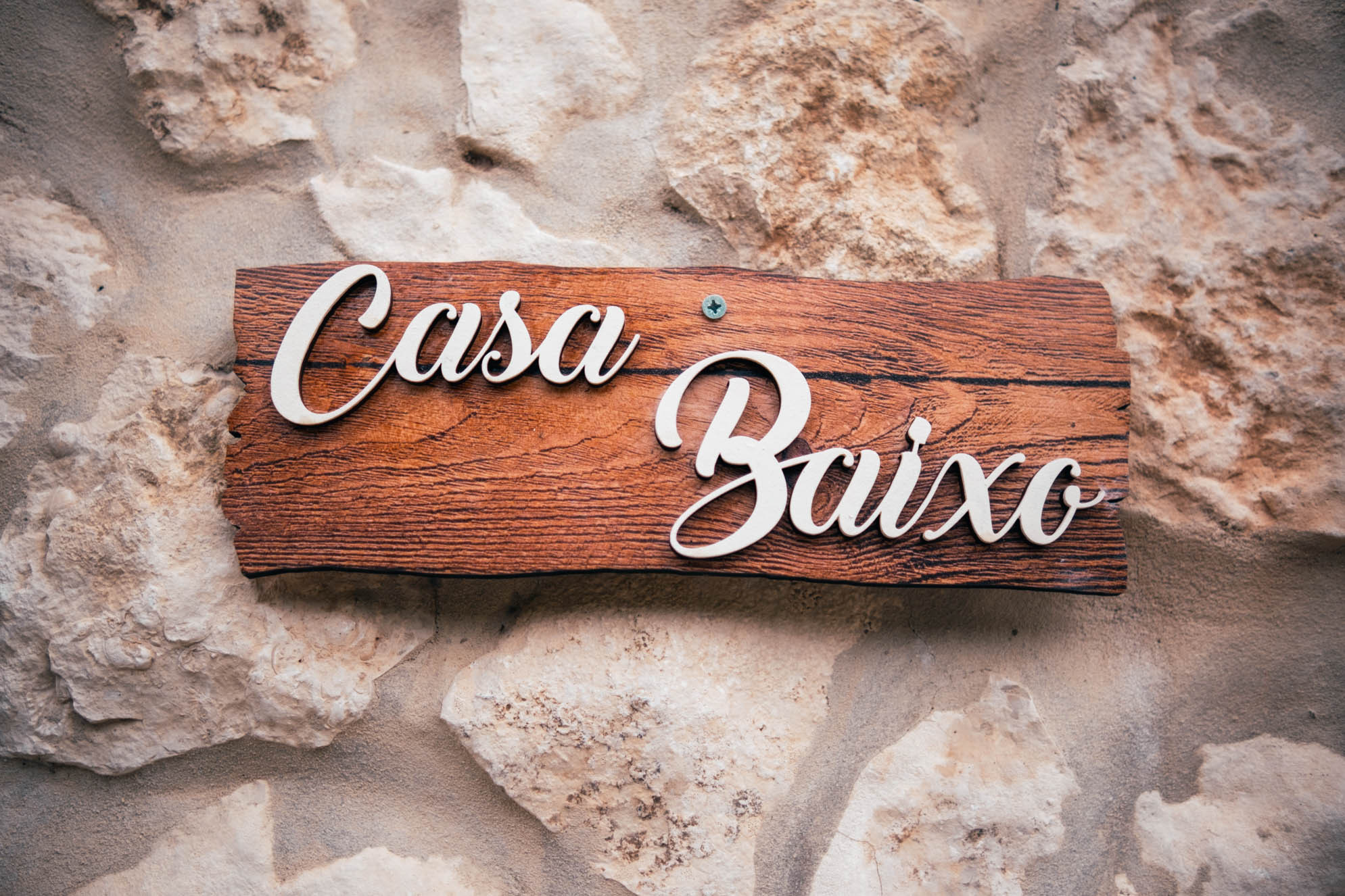 Wooden sign reading "Casa Baixo" mounted on a rough stone wall.