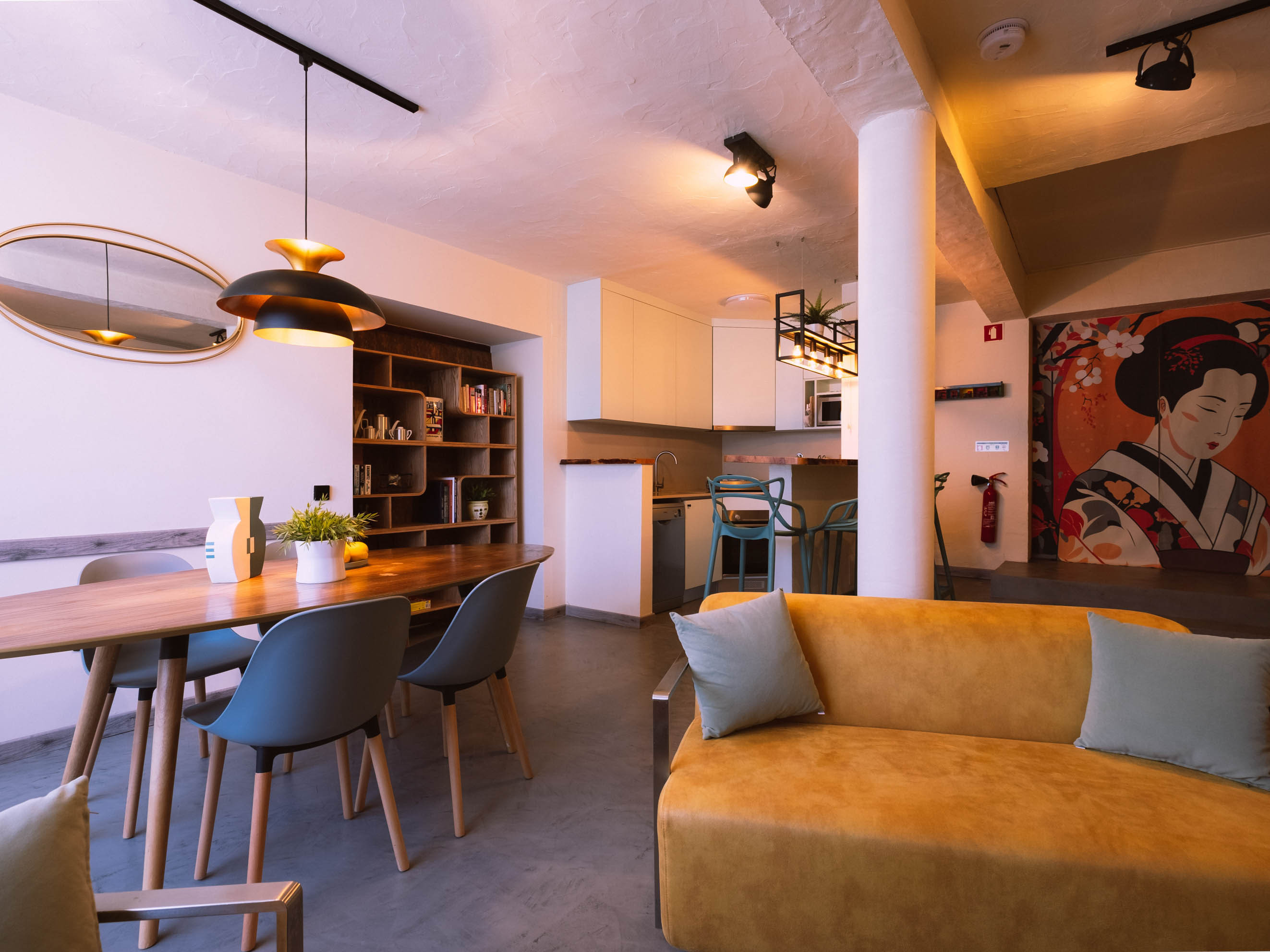 Living space with wooden dining table, blue chairs, yellow sofa, kitchen, and Japanese-style wall art.