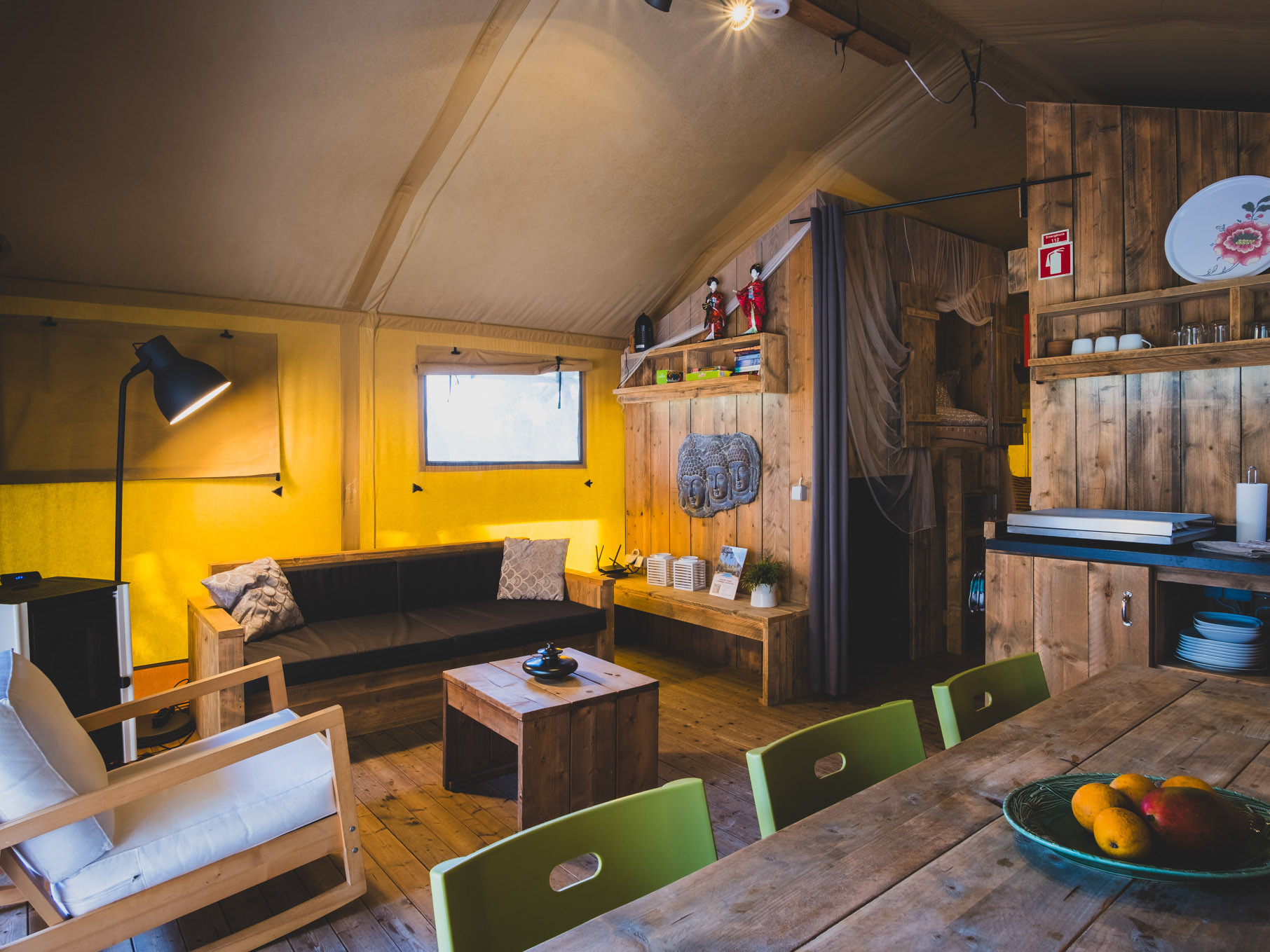 Cozy cabin interior with wooden furniture, yellow walls, sofa, armchair, dining table, and decorative items.