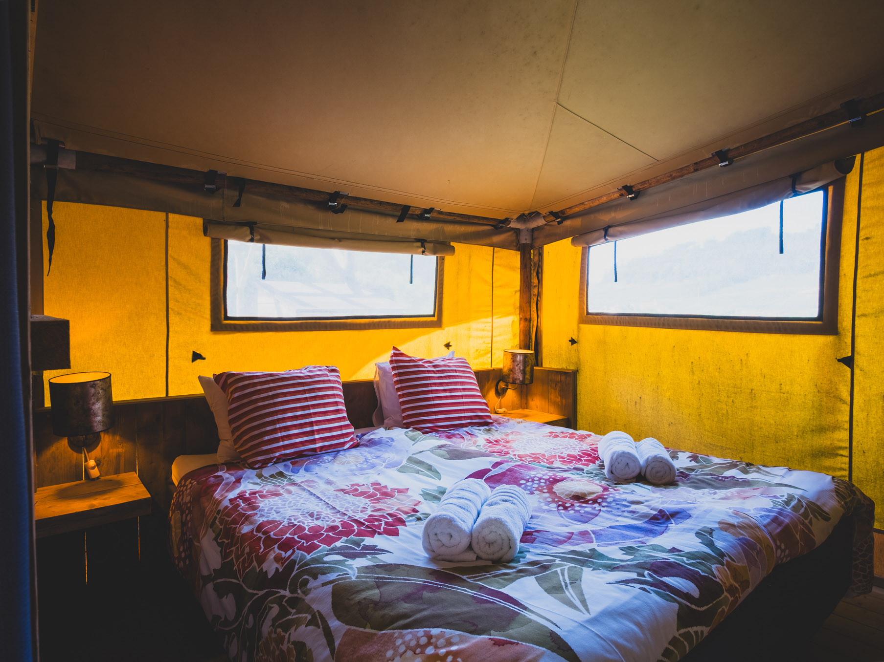 Room with double bed covered by floral and striped bedding inside a tent with yellow walls and two