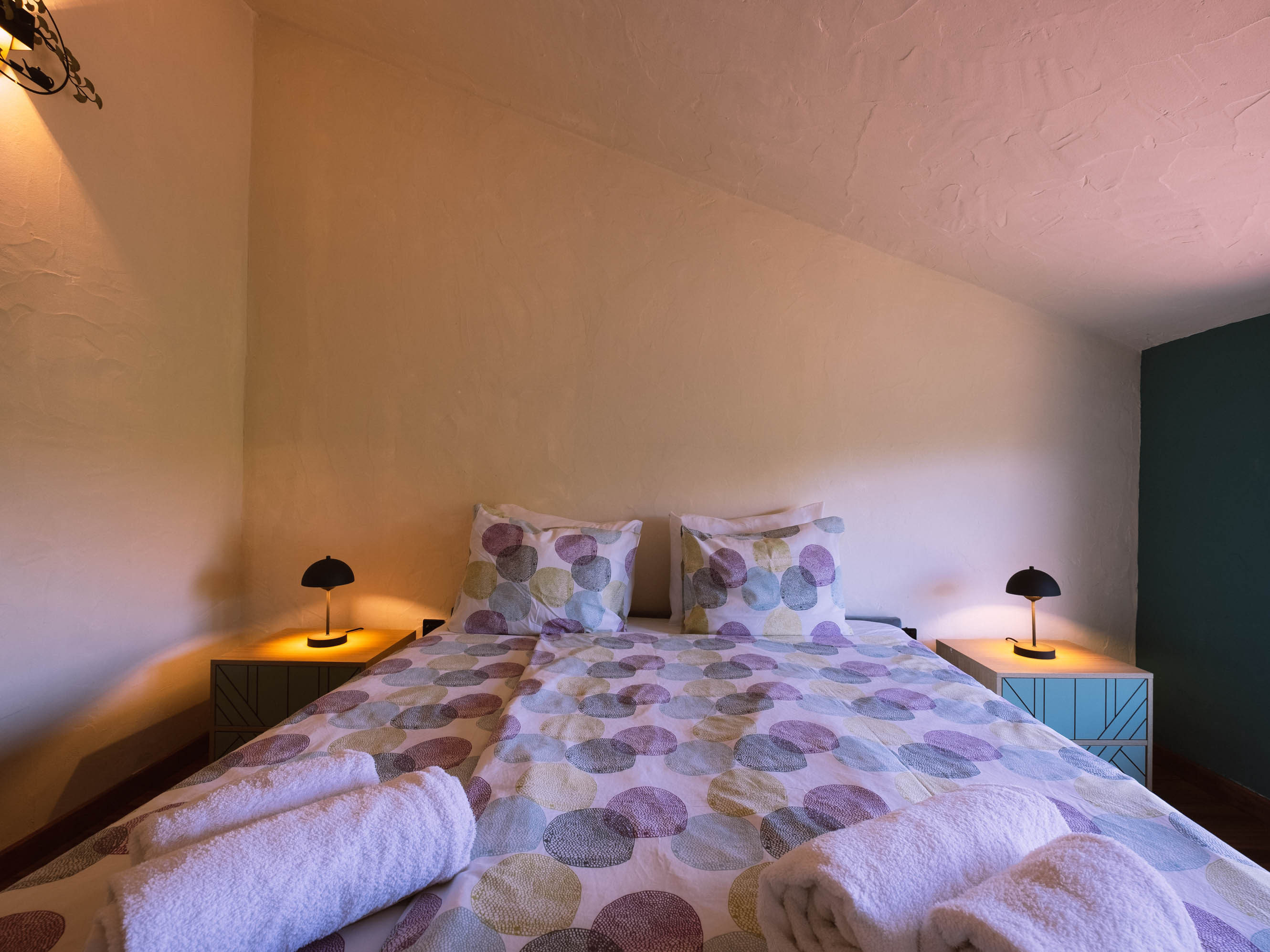 Bed with polka dot bedding, two bedside tables with lamps, and rolled white towels on the bed.