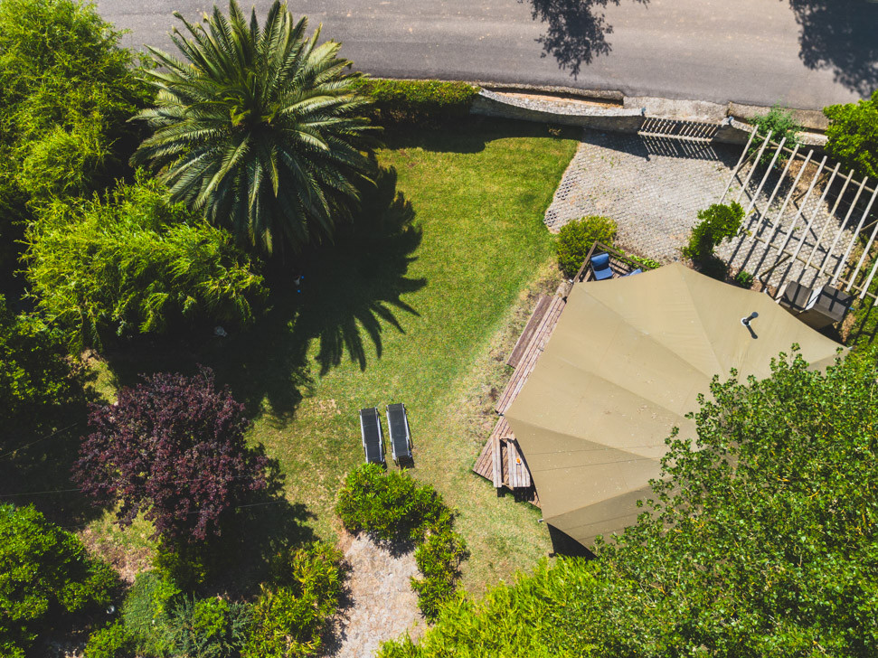 Aerial view of garden with palm tree, two sun loungers, and a beige tent near a road.