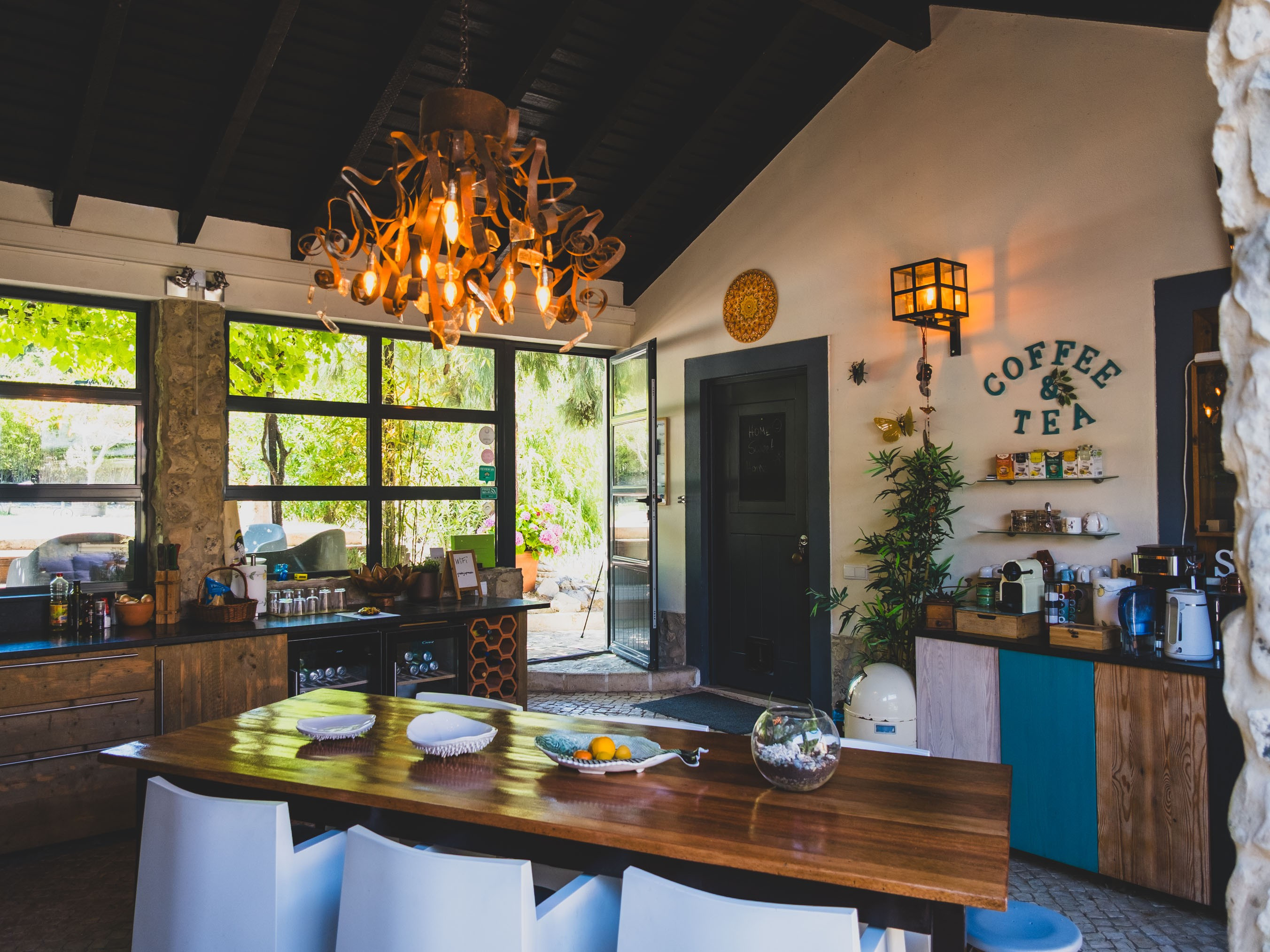 Kitchen with wooden island, white chairs, modern chandelier, coffee and tea corner, and large windows.