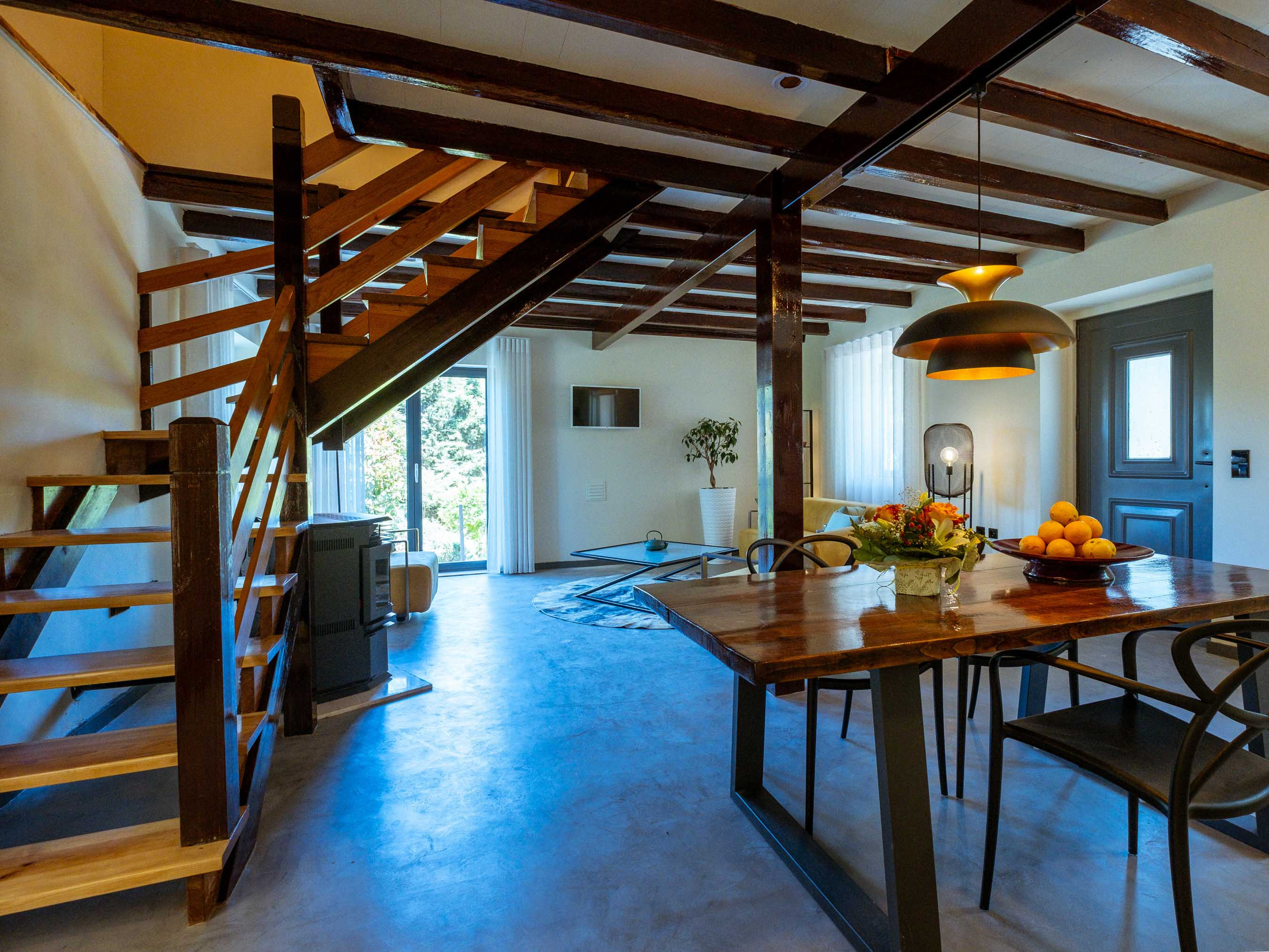 Interior of a living space with wooden staircase, dining table with chairs, and natural light from windows.