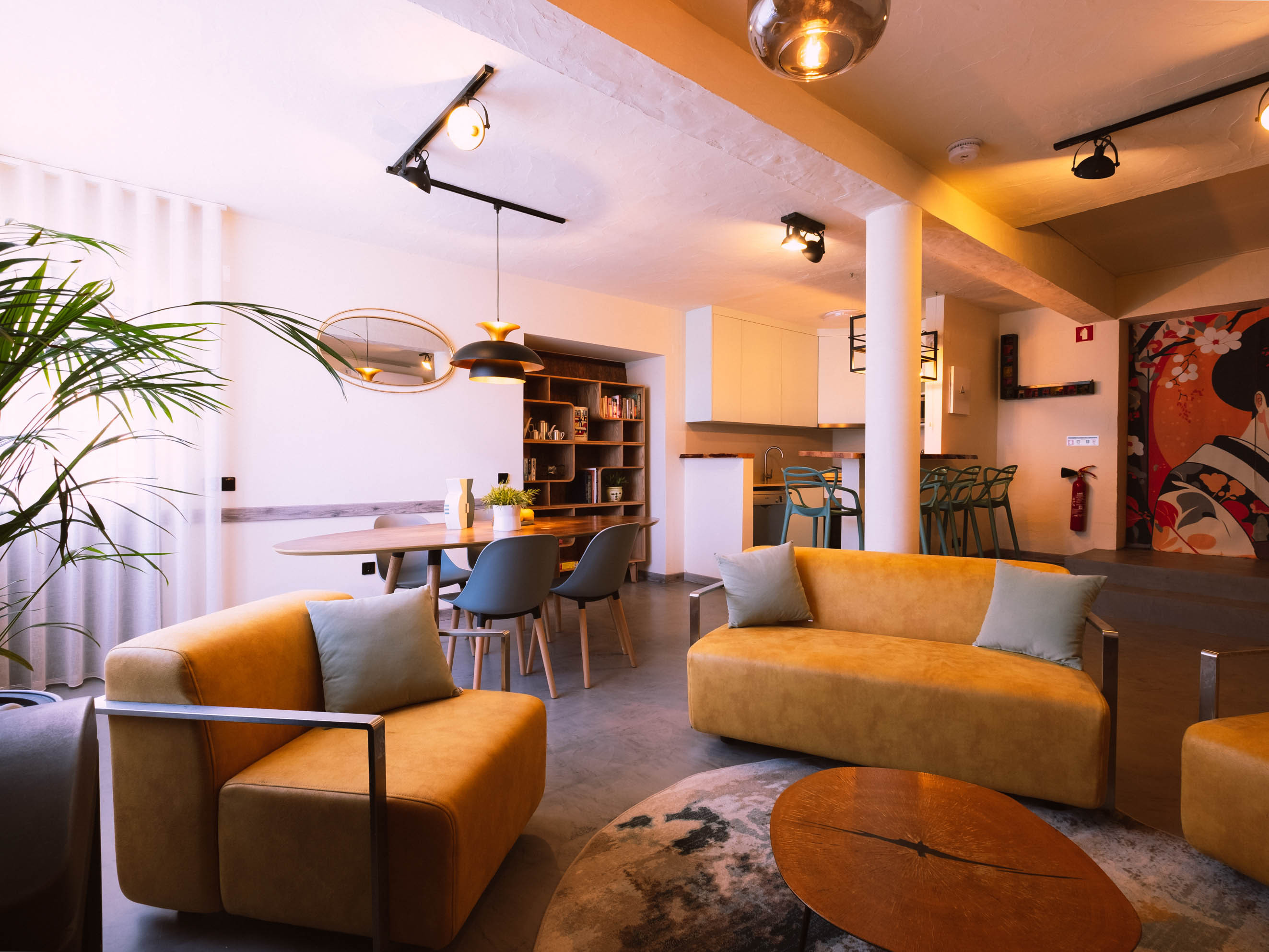 Spacious living area with mustard sofas, gray chairs, round dining table, and indoor plants.