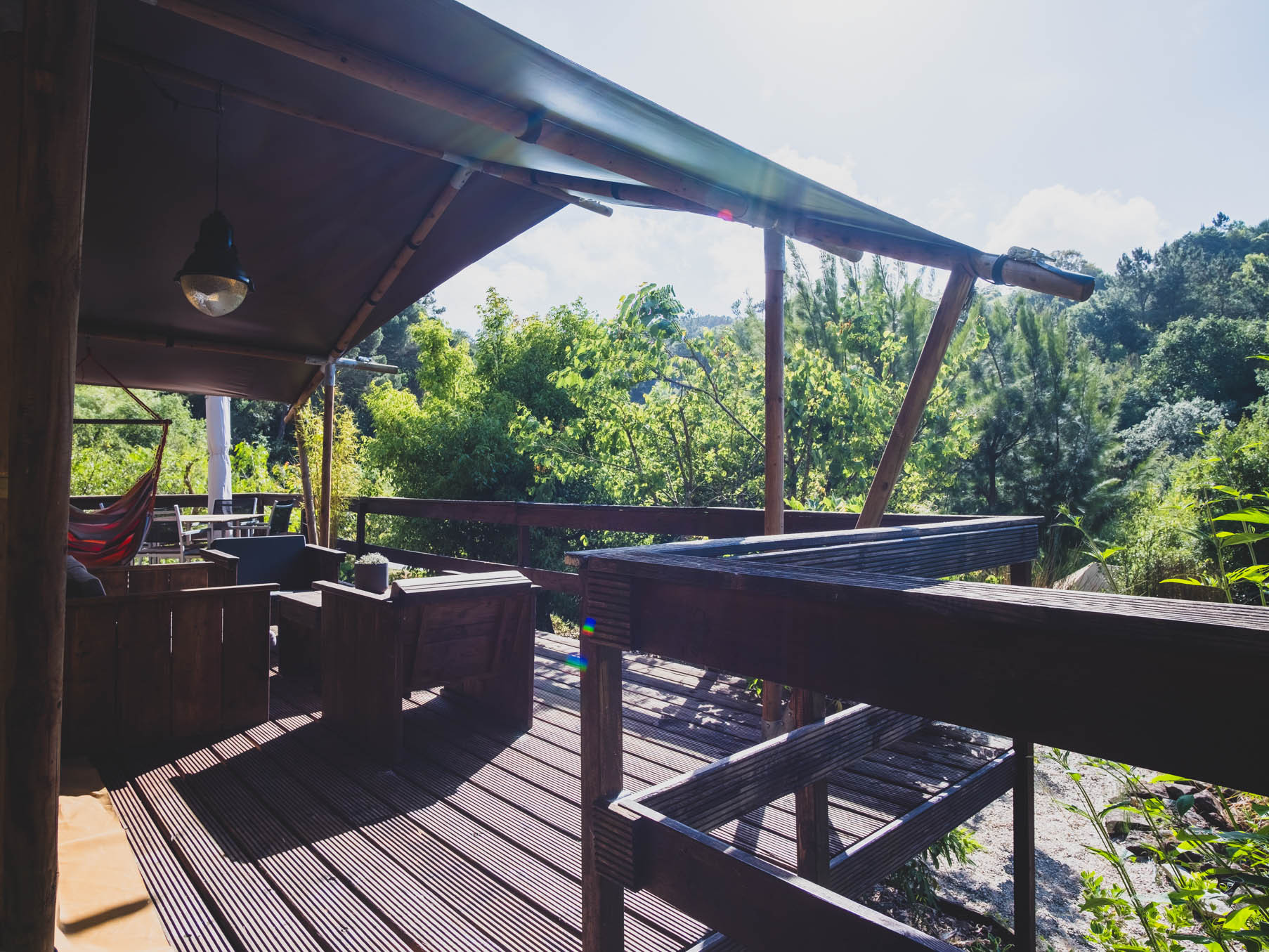 Wooden outdoor deck with seating and green trees in the background under a canopy roof.