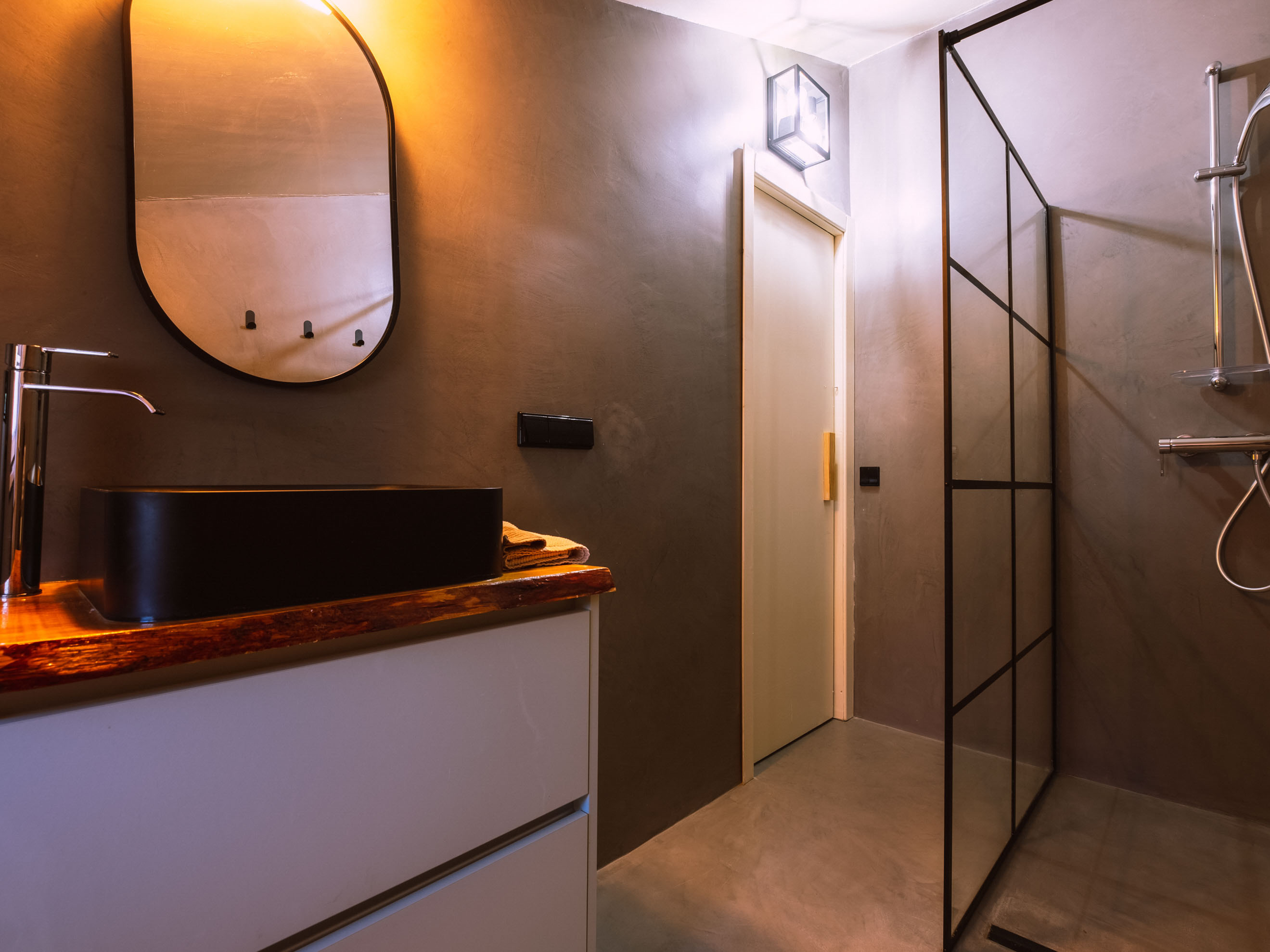 Modern bathroom with black sink, wooden countertop, oval mirror, and glass shower enclosure.