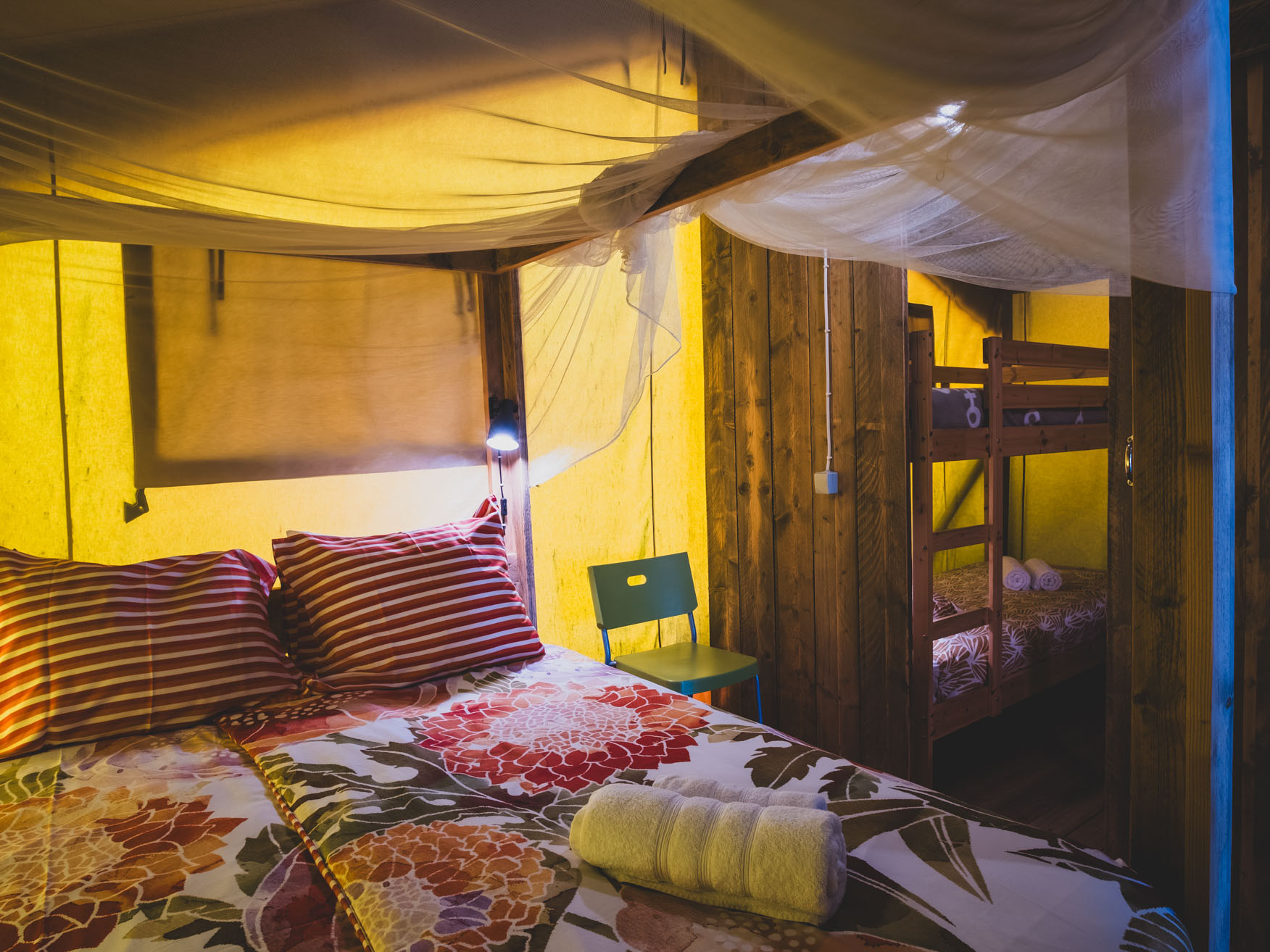 Cozy room with double bed, striped pillows, floral bedspread, green chair, and wooden bunk beds.