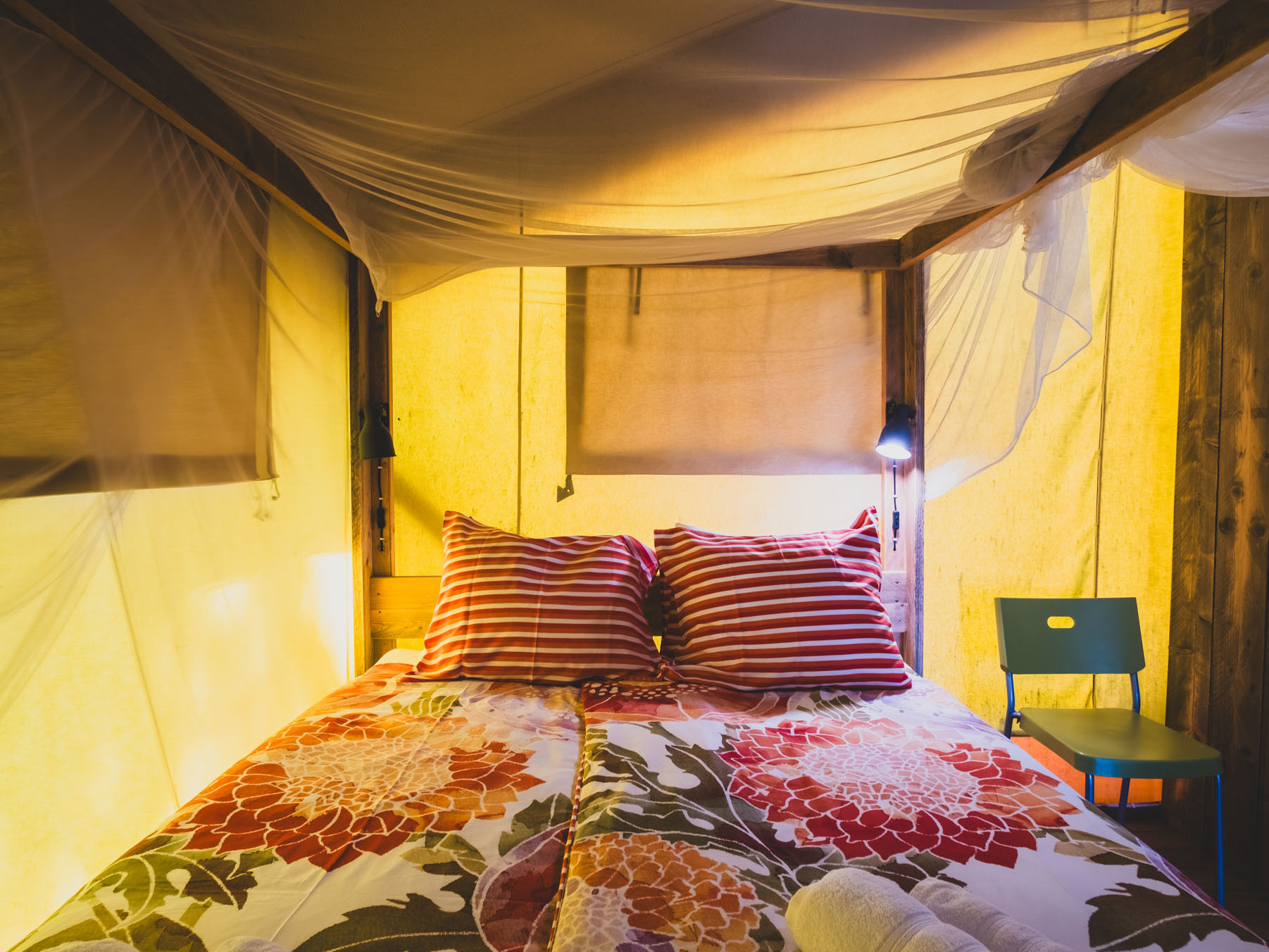 Bed with floral bedspread and striped pillows under canopy in softly lit room.