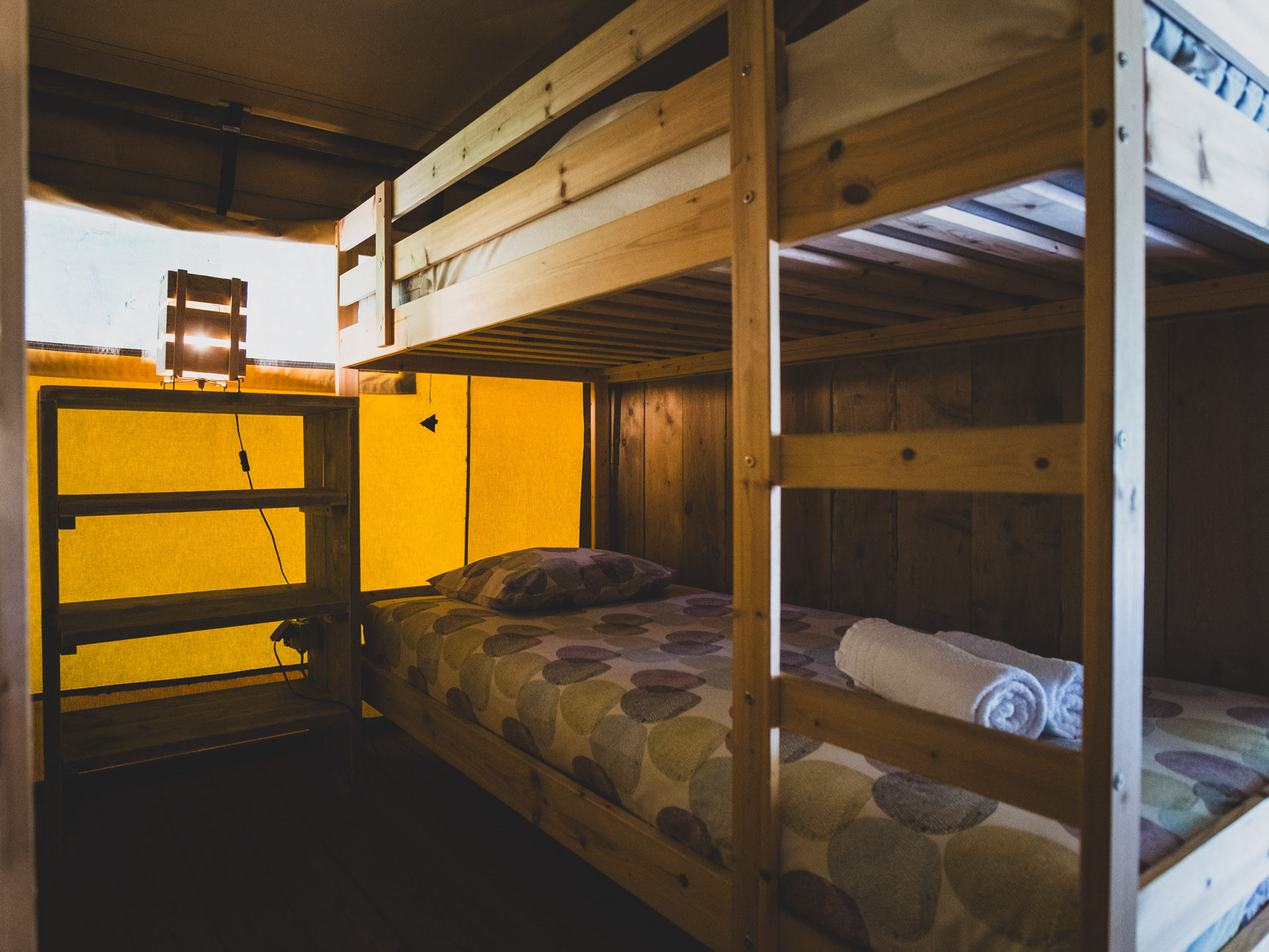 Wooden bunk bed with patterned bedding and rolled towels inside a small cabin with yellow walls.