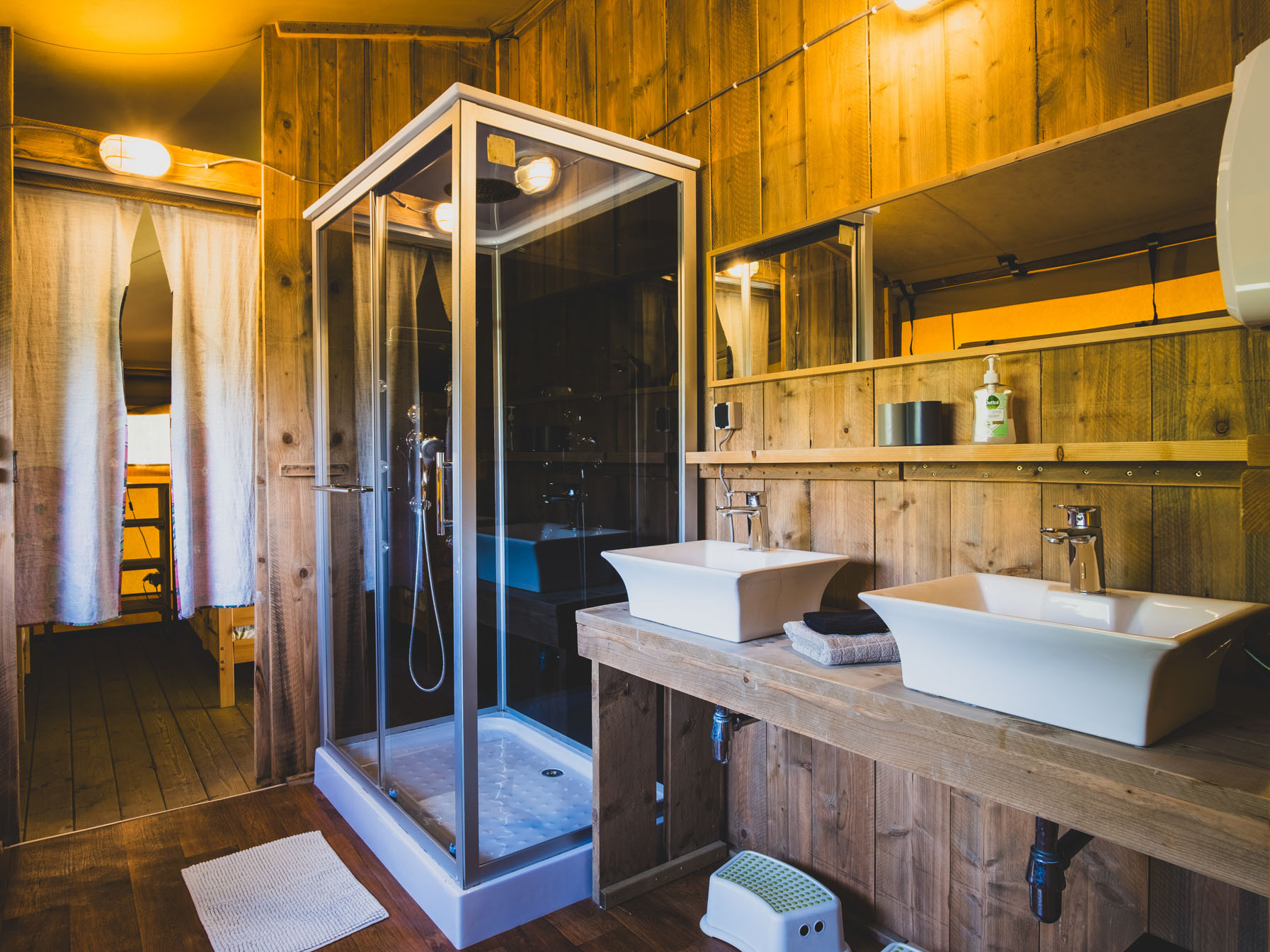 Bathroom with wooden walls, glass shower enclosure, twin white rectangular sinks, and large mirror above.
